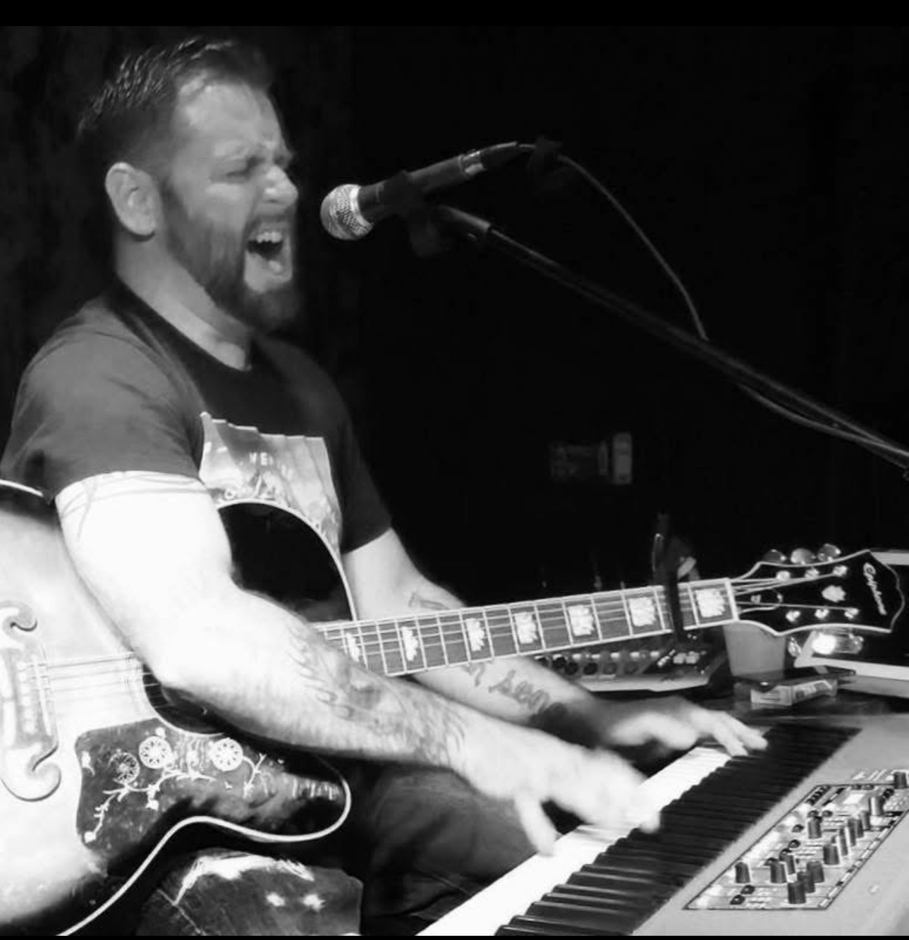 Dan Signor singing at the mic with acoustic guitar and piano